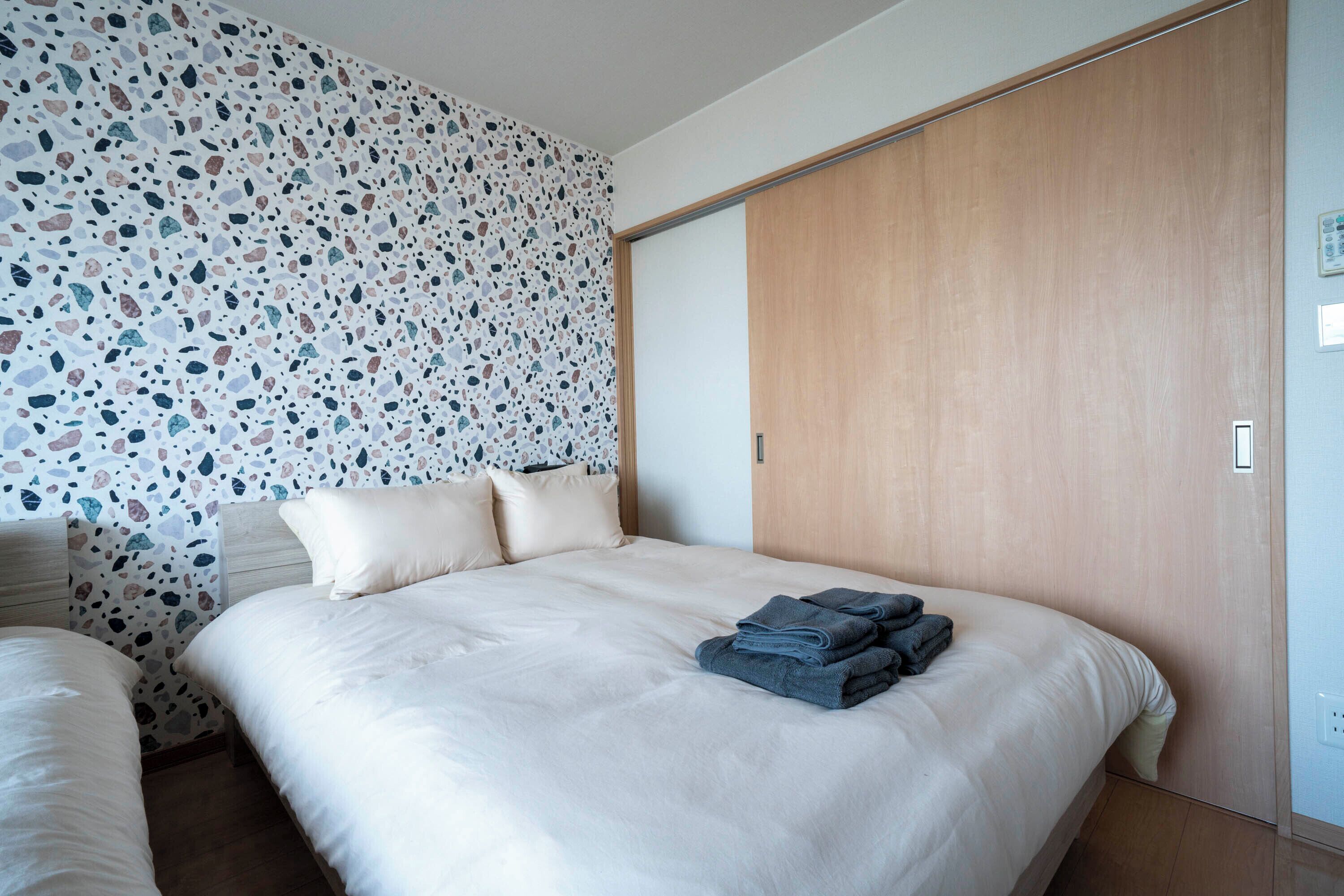 Une chambre à coucher avec un lit, une armoire en bois et un mur orné d’un motif en terrazzo.