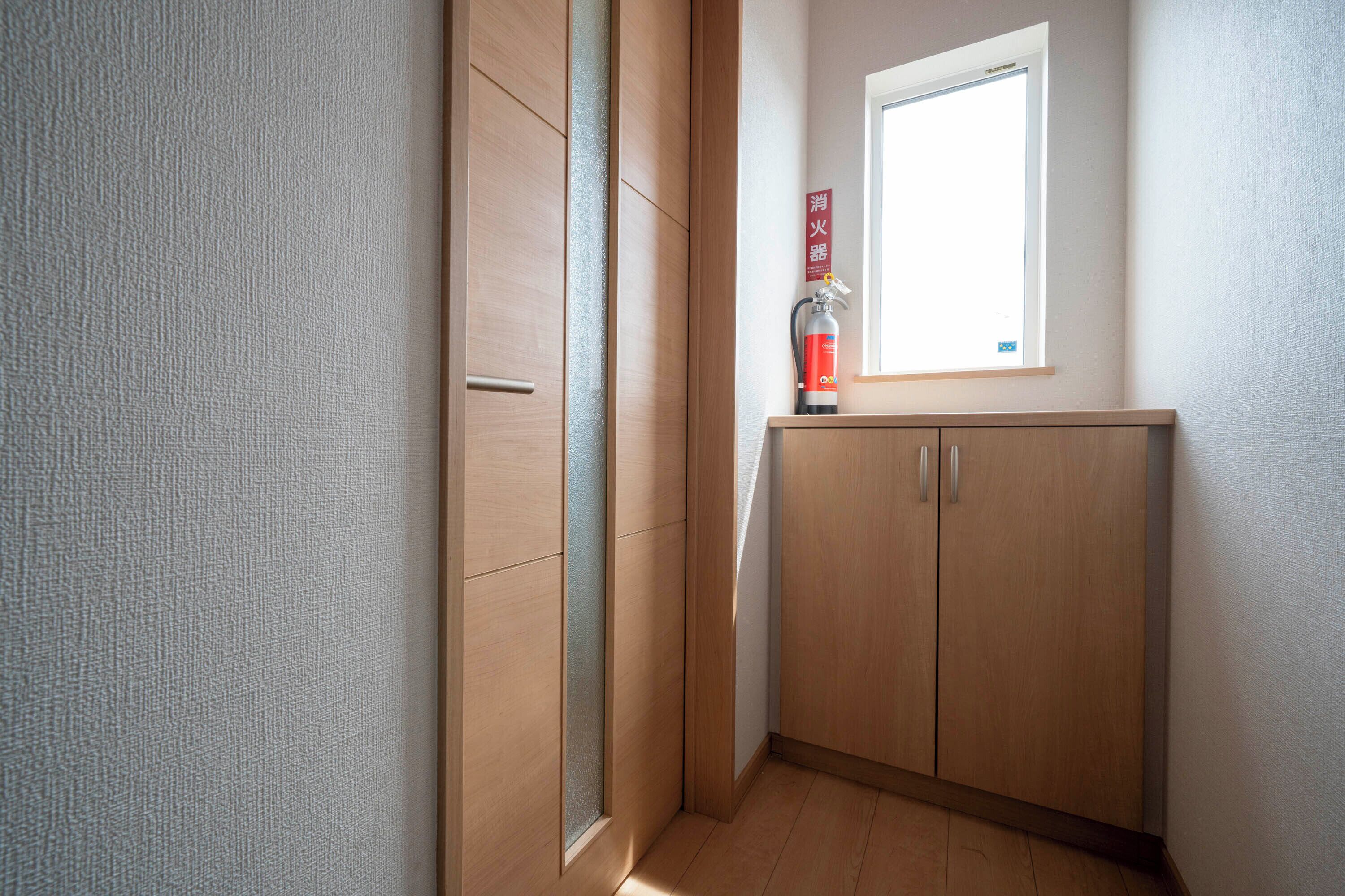 Una esquina de una habitación con un armario de madera, una ventana y un extintor en el alféizar.