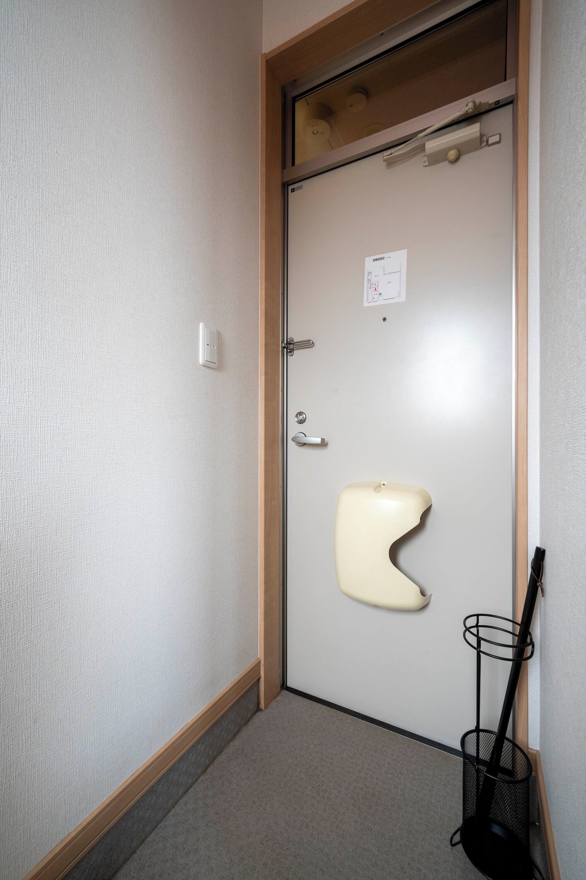 Ein schmaler Gang mit einer Tür, einer Toilette und einem an der Wand angelehnten Besen.