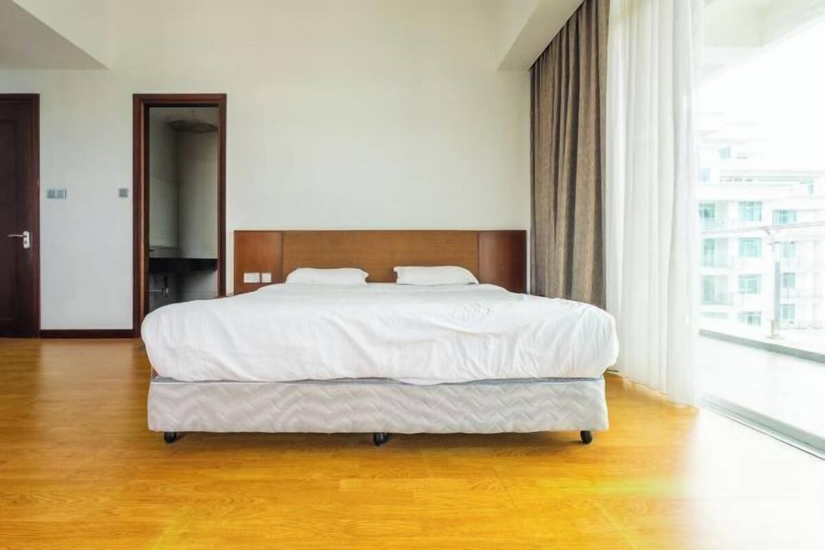 Hotellihuone, jossa on suuri sänky, puulattia, ikkunasta avautuva näkymä ja ovi, joka johtaa toiseen huoneeseen.