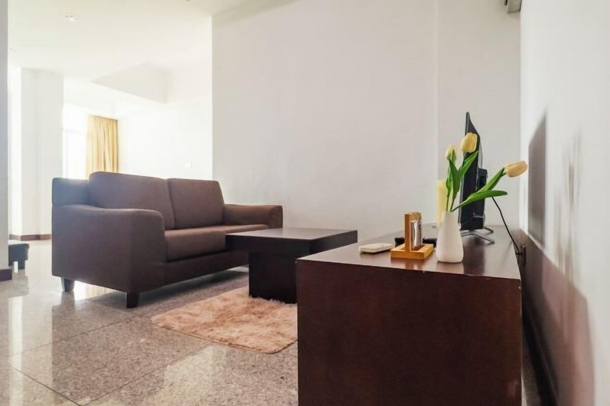 A modern living room with a dark brown sofa, a wooden coffee table, a small rug, and a vase with flowers on a wooden side table.