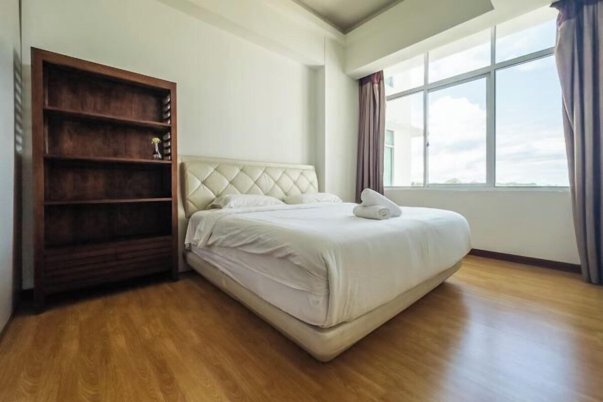 A bedroom with a bed, a wooden wardrobe, and a large window.