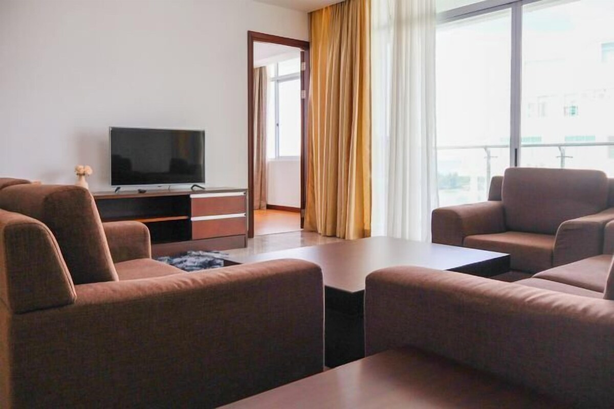 A modern hotel room with a flat-screen TV, a sofa set, a coffee table, and a large window with curtains.