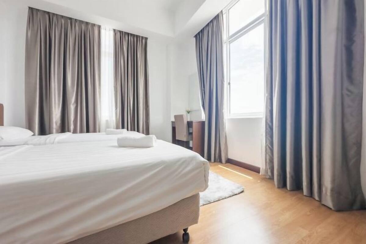 Hotellihuone, jossa on suuri sänky, yöpöytä, ikkuna verhoilla ja näkymä ulos.