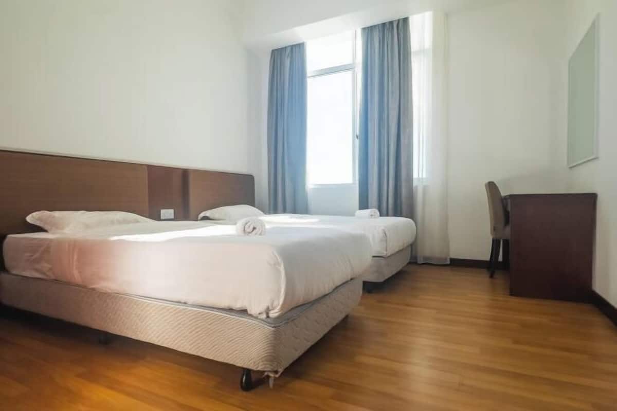 Hotellihuone, jossa on kaksi sänkyä, puulattia, työpöytä ja ikkuna, jossa on verhot.