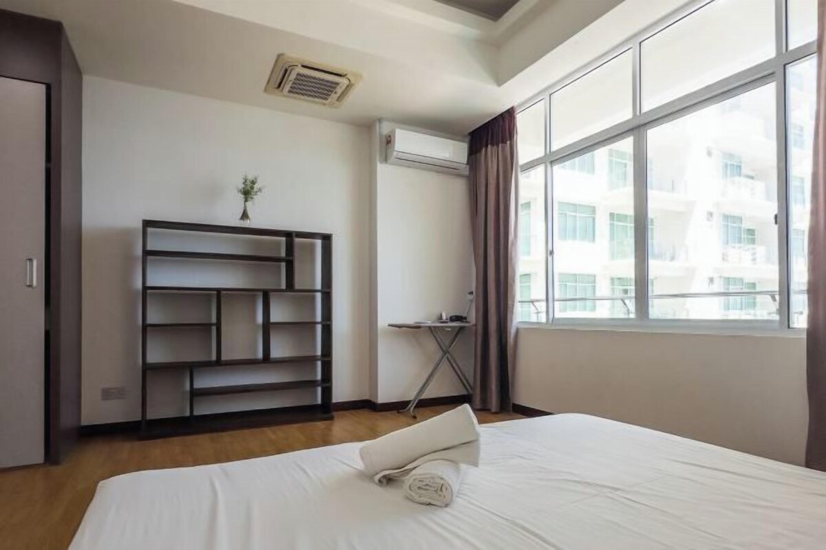 A hotel room with a bed, a desk, a shelf unit, and a window with a view of buildings.