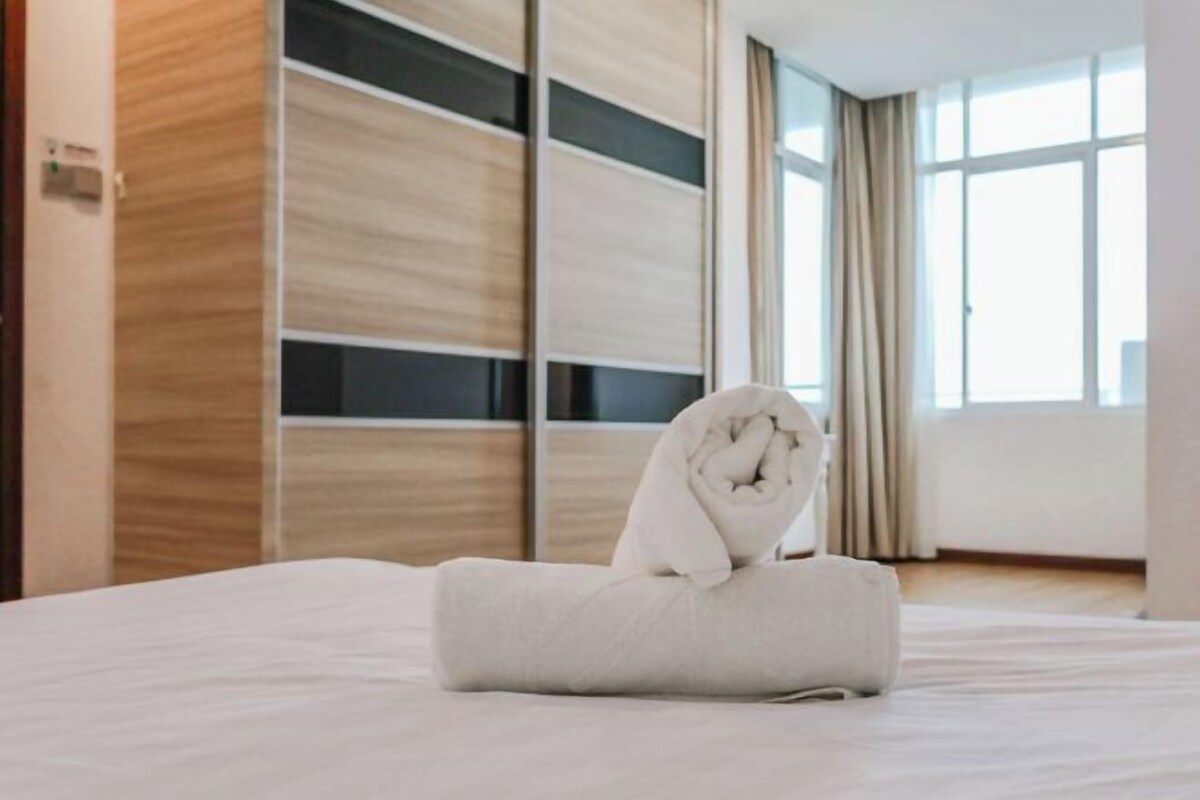 A hotel room with a neatly made bed, a window with curtains, and a wooden panel wall.