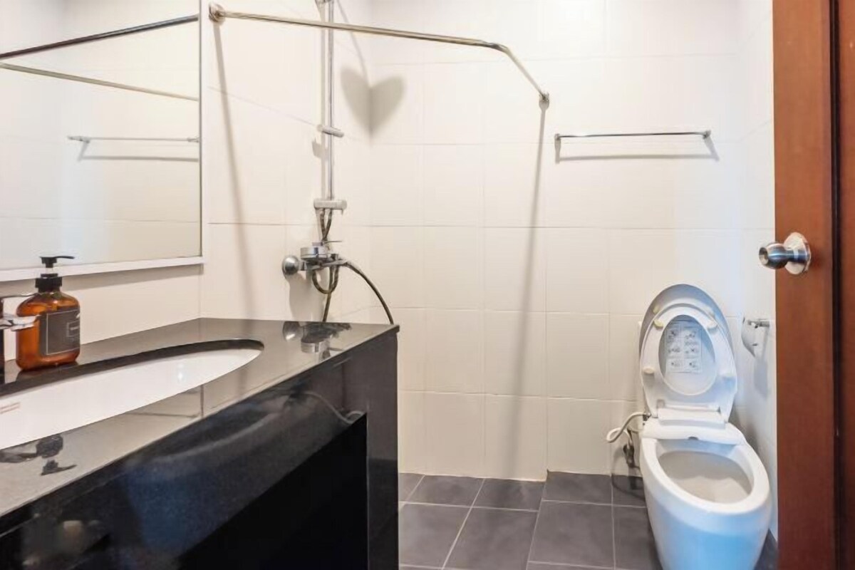 A bathroom with a black sink, a white toilet, a shower area, and a mirror.