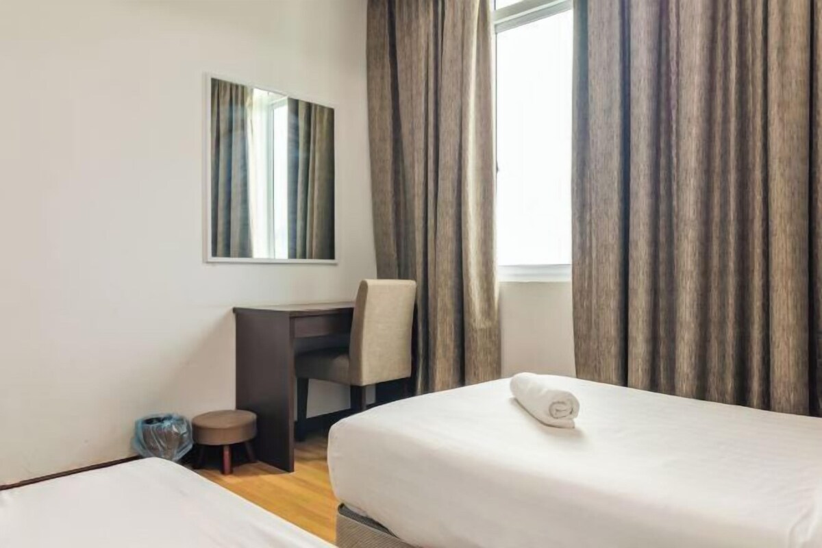 A hotel room with two beds, a desk, a chair, a small stool, a mirror, and a window with curtains.