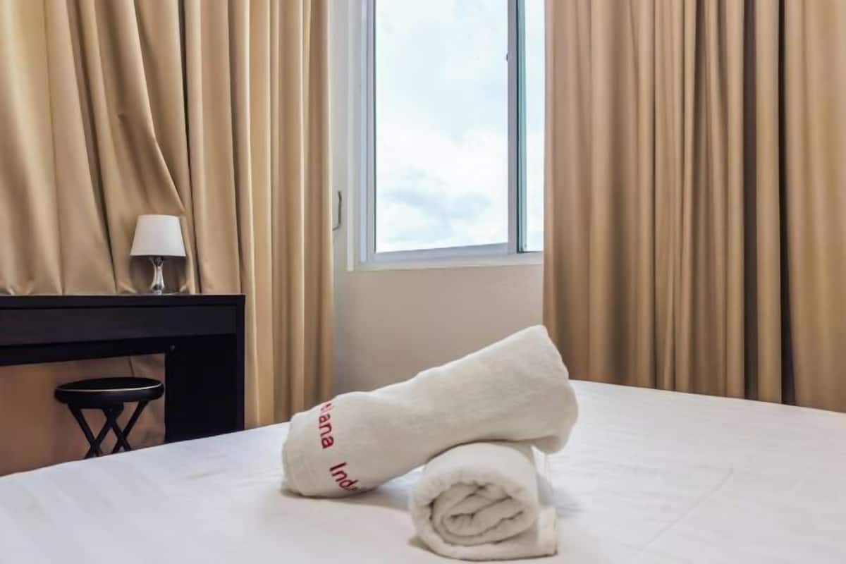 Hotellihuone, jossa on sänky, lamppu, ikkuna ja verhot.