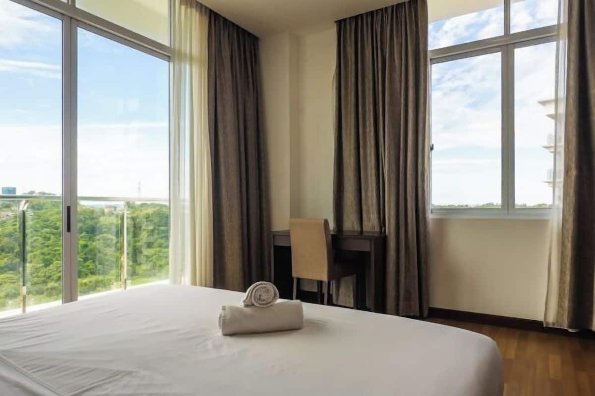 Hotellihuone, jossa on suuri sänky, työpöytä ja ikkunoista avautuva näkymä vehreään maisemaan.