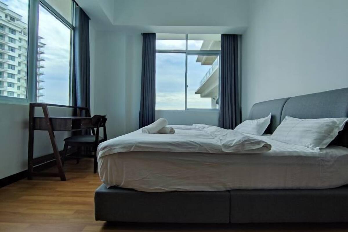 Moderni hotellihuone, jossa on suuri sänky, työpöytä ja suuri ikkuna, josta avautuu näkymä rakennukseen.