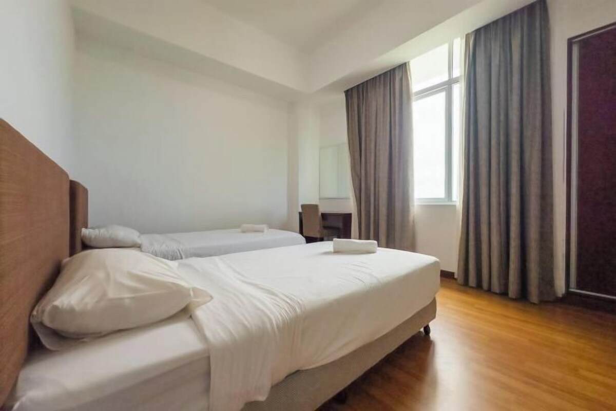 A hotel room with two beds, a wooden headboard, a window with curtains, and a wooden floor.