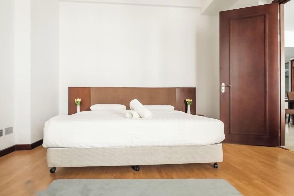 A hotel room with a bed, a wooden door, and a view of the hallway.