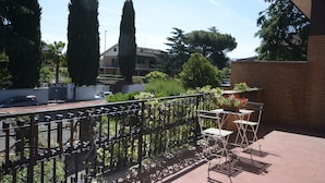 A balcony with a wrought iron fence, a table with chairs, and potted plants. - Casa Di Silvana (Rome)