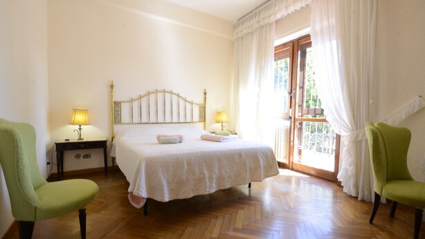 A bedroom with a bed, two bedside lamps, a nightstand, and two chairs. - Casa Di Silvana (Rome)