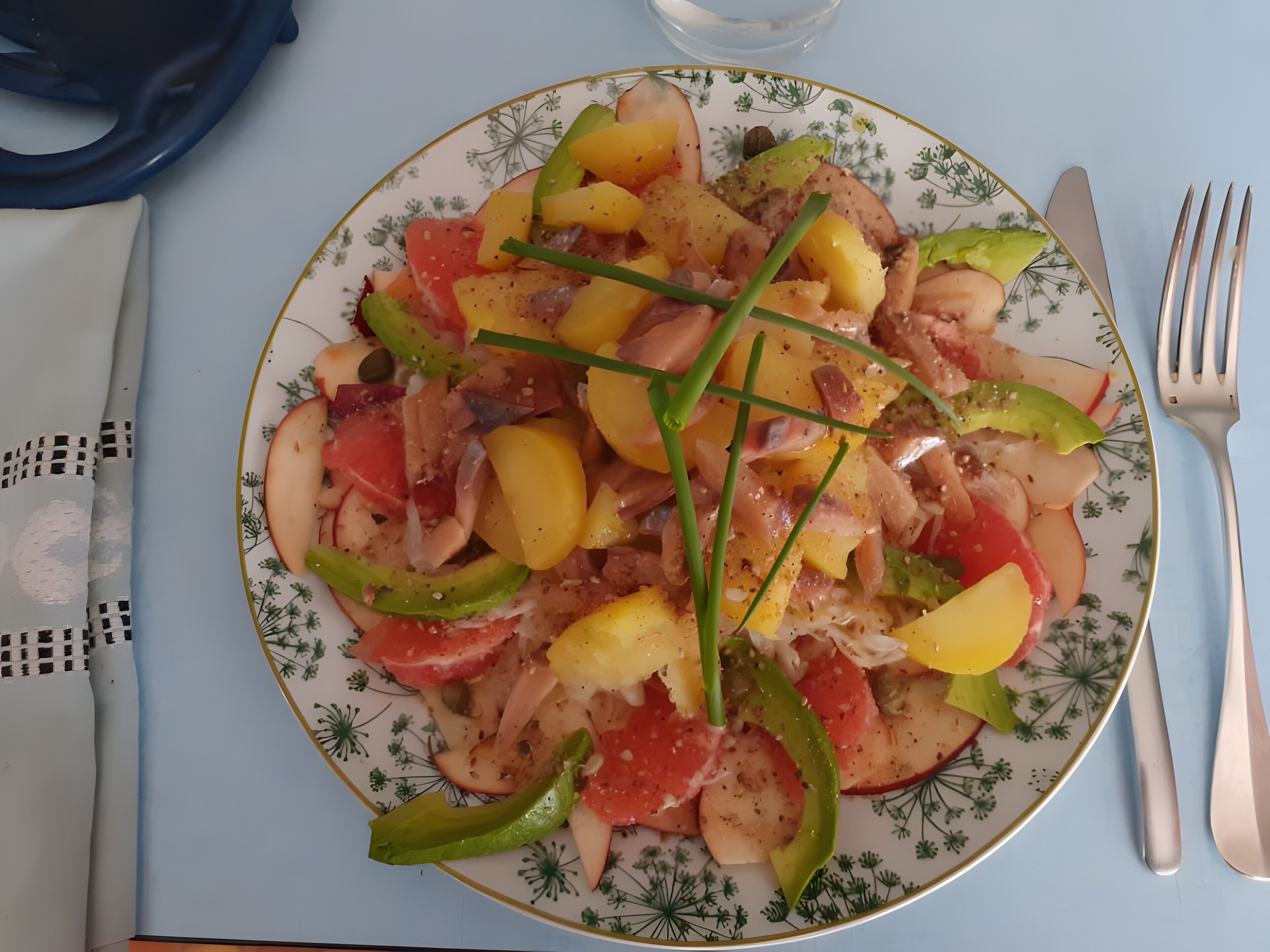 Une assiette remplie de divers légumes et de viande, accompagnée de couverts et d’une nappe à motifs.