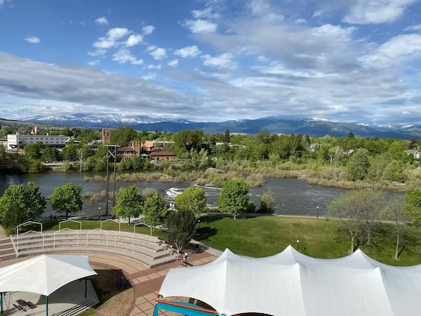 Vista al río con un anfiteatro junto al río, un espacio con carpas blancas y montañas al fondo.