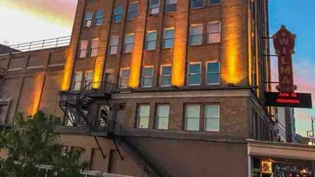 Um edifício de vários andares com fachada de tijolos, janelas amplas e um escape de incêndio bem visível.