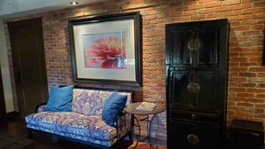 Quarto com sofá, uma mesa pequena, um quadro emoldurado e um armário em frente a uma parede de tijolos.