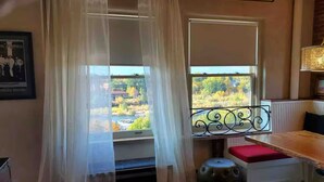Quarto com janela dando para um jardim, um banco branco com almofada vermelha e um quadro pendurado na parede.
