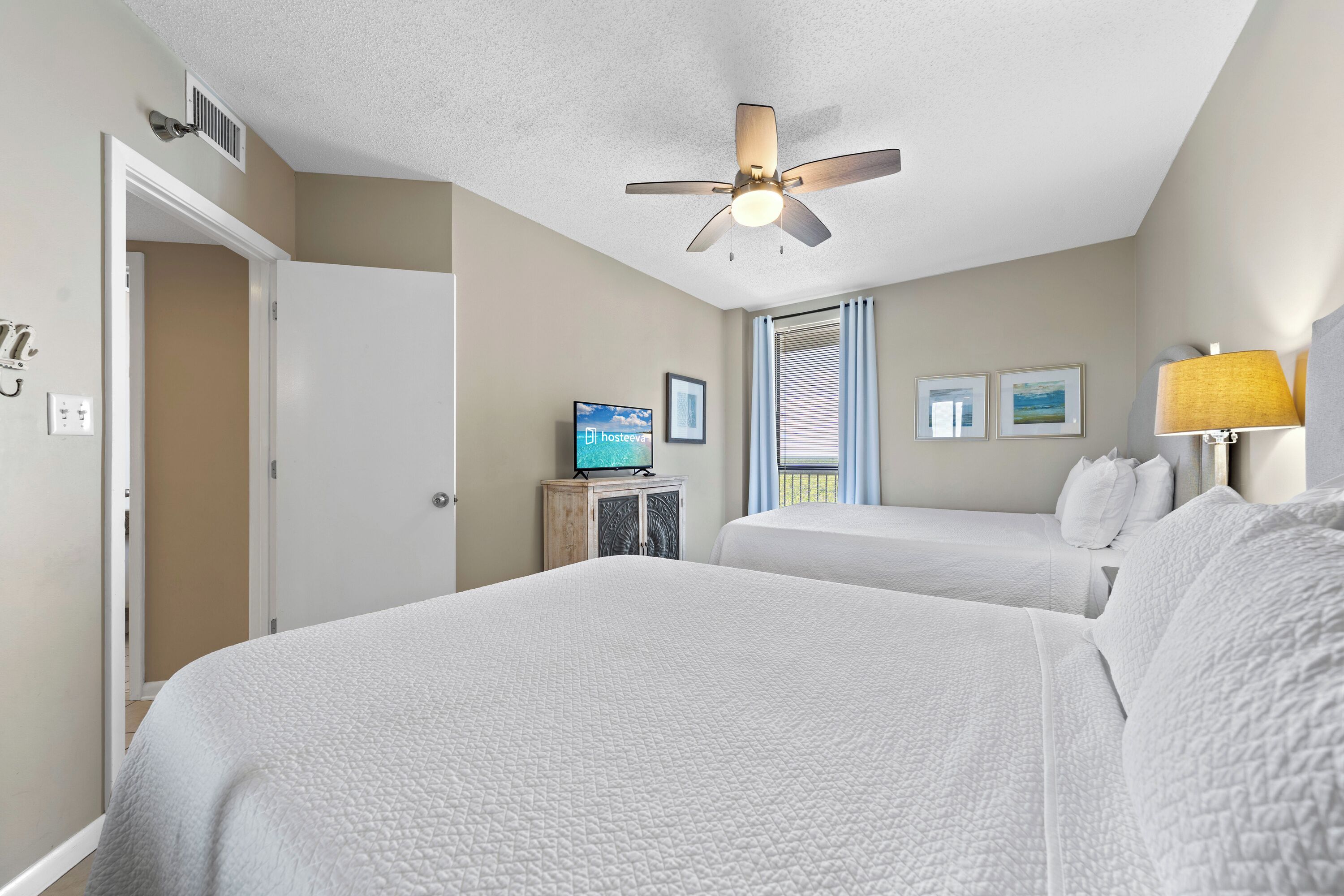 A hotel room with two beds, a ceiling fan, a television on a wooden cabinet, and a window with blinds.