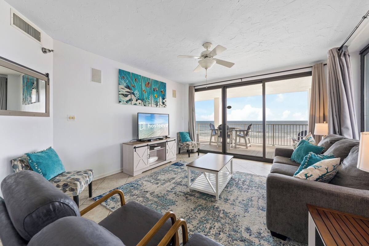 A modern living room with a television, comfortable seating, a ceiling fan, and a view of the outdoors.