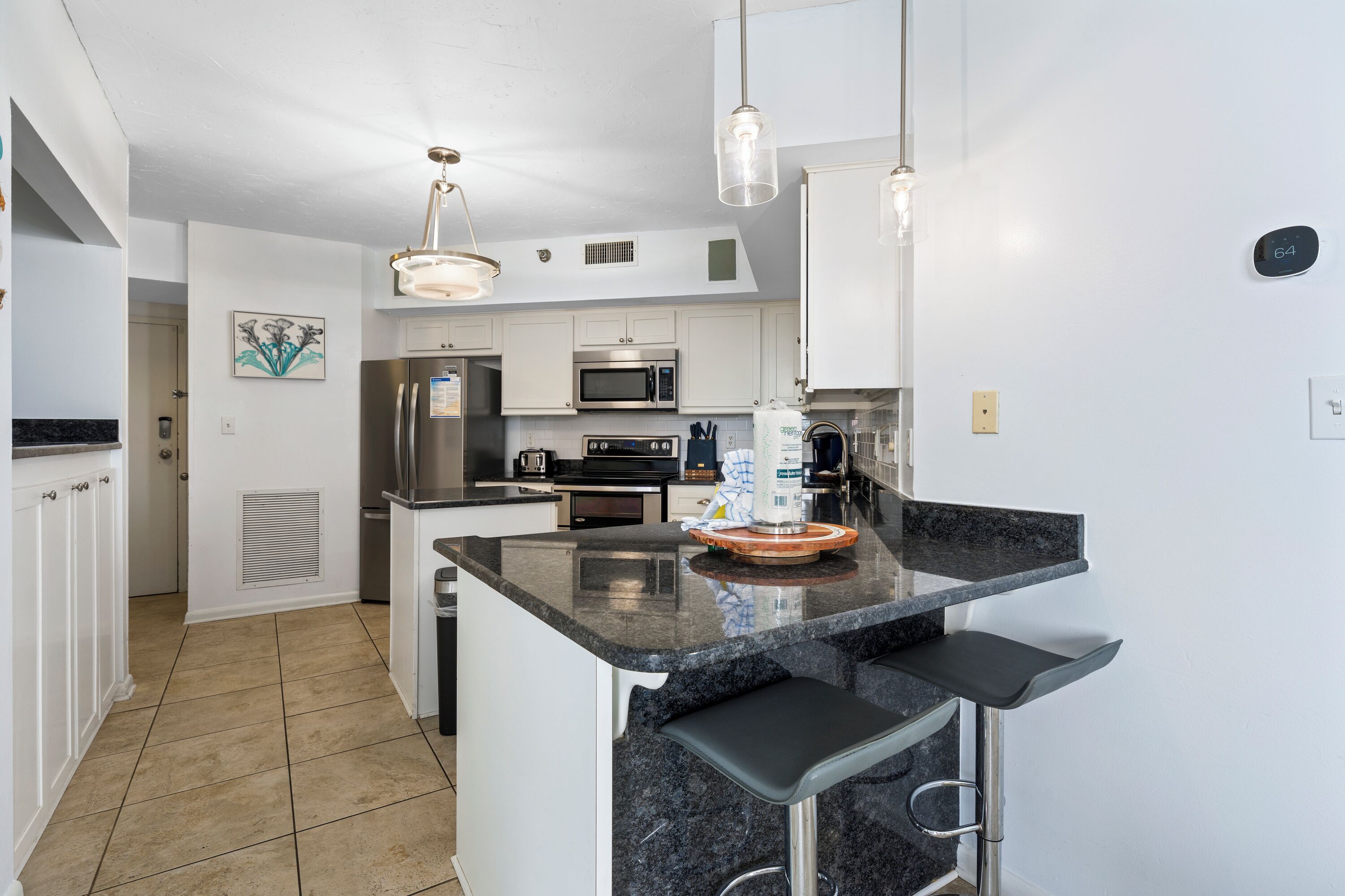 A modern kitchen with white cabinetry, a central island with bar seating, stainless steel appliances, and pendant lighting.