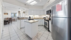 Una cocina moderna con armarios blancos, una isla central, electrodomésticos de acero inoxidable y un tragaluz.