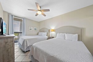 A hotel room with two beds, a ceiling fan, a TV, and a balcony with blinds.