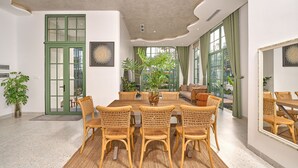 A dining area with a round table and wicker chairs, a green door, and large windows with curtains. - Luxury 4 bedroom Solar Villa (Phu Quoc)