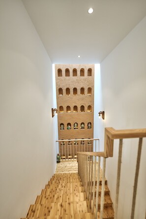 Un escalier avec des marches en bois et une rampe en bois, menant à un mur percé de nombreuses petites fenêtres.