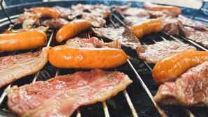 Ein Grill mit verschiedenen Fleischsorten und Würstchen, die im Freien zubereitet werden.