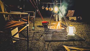 Ein Campingplatz mit Grill, Laterne und Töpfen, die über dem Feuer hängen.