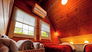 Ein gemütliches Zimmer mit Holzwänden, zwei Betten mit roter Bettwäsche, einem gewebten Korb mit Handtüchern und einem Fenster mit Jalousien.