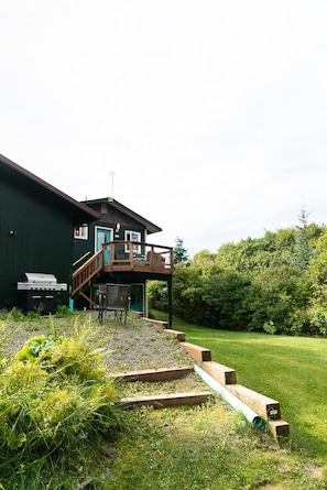 A house with a deck, a grill, and a staircase leading to a covered area.