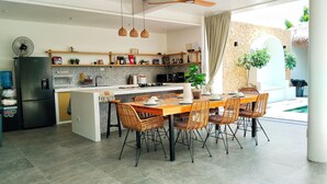 Une cuisine moderne dotée d’un îlot central, d’un coin repas avec des chaises en osier et d’une vue sur une piscine.
