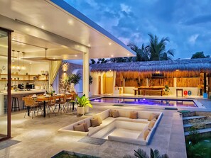 Un área exterior moderna con piscina, comedor y una estructura de techo de paja.
