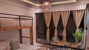 Une chambre moderne avec un lit superposé, un lit simple, un coin repas avec des chaises et une grande fenêtre avec des rideaux.