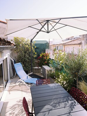 A patio with a table and chairs, a blue lounge chair, and a large umbrella providing shade.