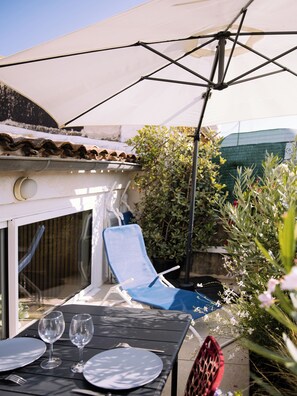 A patio with a table set for two, a blue lounge chair, and a white umbrella.