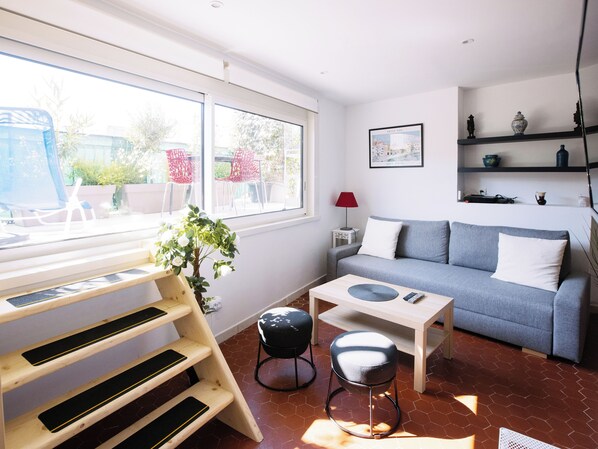 A modern living room with a grey sofa, a wooden coffee table, a red lamp, and a staircase with black mats.