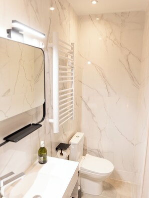 A modern bathroom with a white marble backsplash, a toilet, a sink with a soap dispenser, and a towel rack.