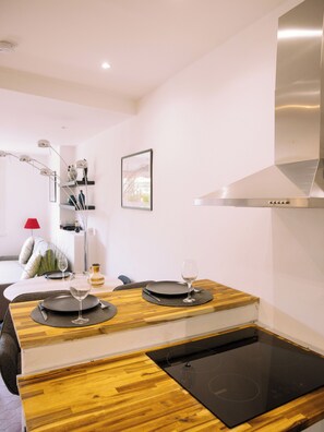 Una cocina moderna con una placa de inducción integrada, un extractor de acero inoxidable y una zona de comedor con una mesa de madera preparada para dos comensales.