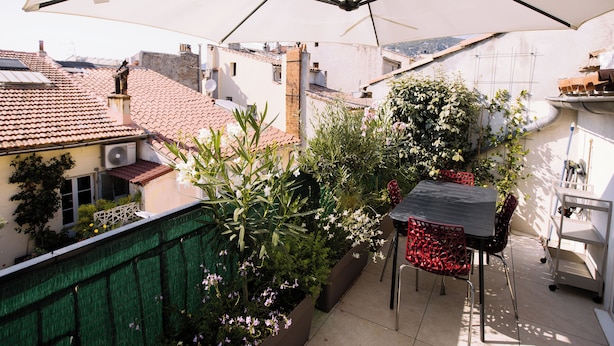 Une terrasse sur le toit, avec une table et des chaises placées sous un grand parasol, entourée de plantes et de fleurs en pot.