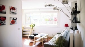 Un salon moderne comprenant un canapé, une table basse et un coin repas avec un banc. On y trouve également des œuvres d’art murales et une grande fenêtre qui laisse entrer la lumière naturelle.