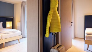 A hotel room with a bed, a suitcase, and a coat hanging on the wall. - Hotel UND smart alpine stay (Schladming)