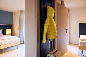 A hotel room with a bed, a suitcase, and a coat hanging on the wall.