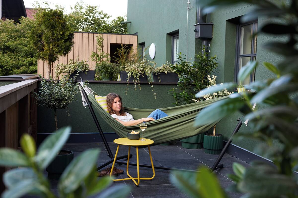 A person relaxing in a hammock on a rooftop terrace with a small table and potted plants.