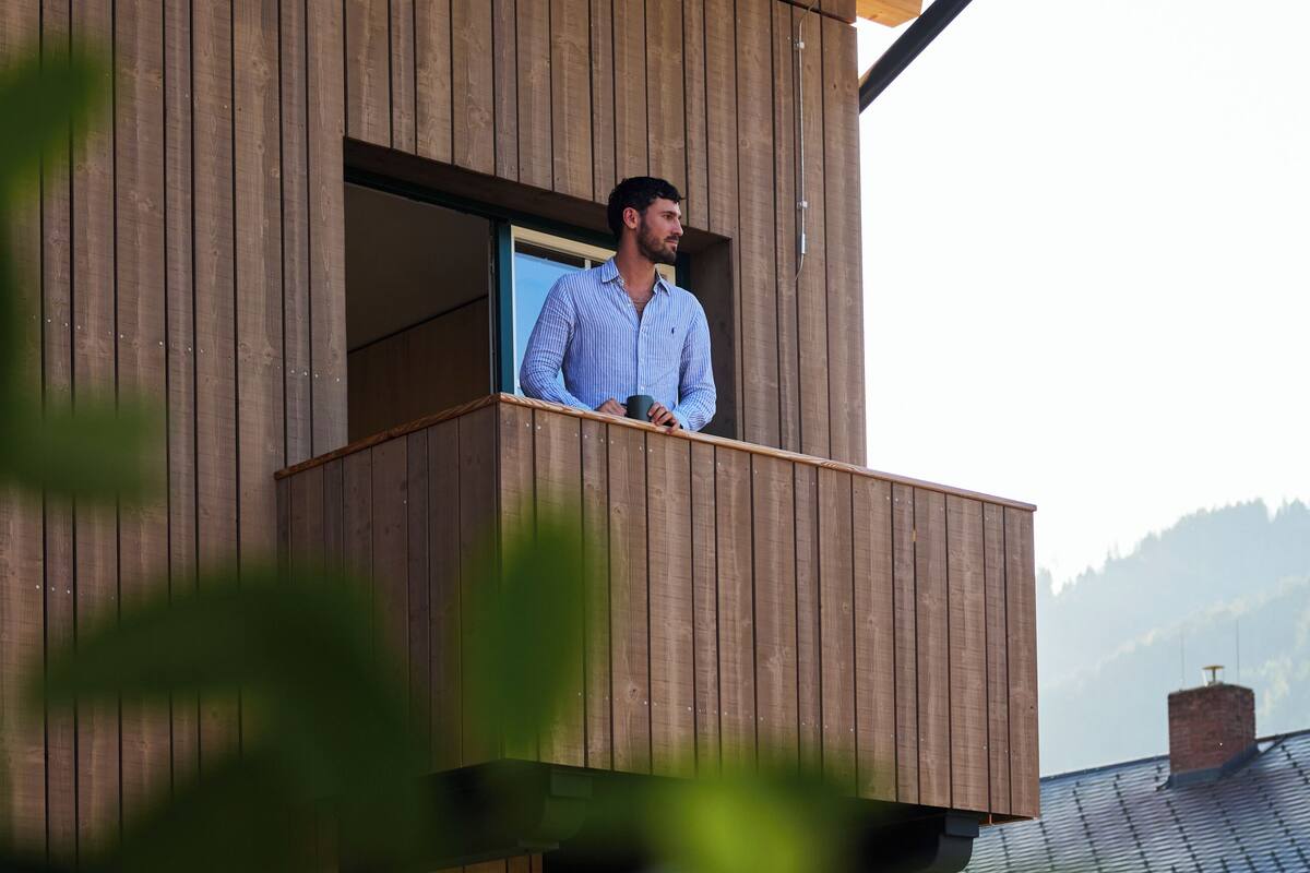 A person standing on a balcony of a wooden building with a window.